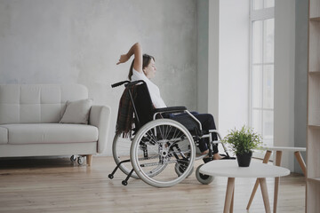 Young brunette caucasian woman sitting on wheelchair and dancing. She is singing song while...