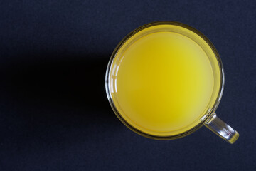 A glass mug filled with pineapple or orange juice, or mango juice is placed on a dark surface. View from above. Minimalism. Free space for an inscription
