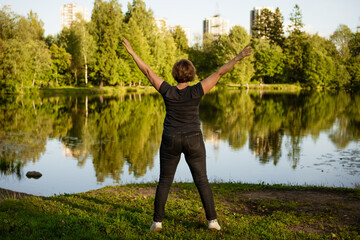 Fototapeta na wymiar Adult woman doing exercises by the lake in the park on a summer day