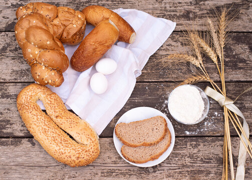 Fresh crispy bread and two eggs on white napkin with spikelets of wheat, bowl of flour, bread on plate on wooden table. Harvest season holiday World Bread Day. Bread is the staff of life. Top view.