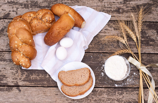 Fresh crispy bread on white napkin with spikelets of wheat, bowl of flour and for bread on plate on wooden table. Harvest season holiday World Bread Day. Bread is the staff of life. Top view.