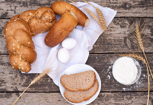 Fresh crispy bread and two eggs on white napkin with spikelets of wheat, bowl of flour, bread on plate on wooden table. Harvest season holiday World Bread Day. Bread is the staff of life. Top view.