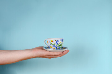 Hand and cup on blue background. Man holding White cup with pain