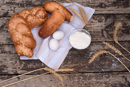 Fresh crispy bread on white napkin with spikelets of wheat, bowl of flour and two eggs on wooden table. Harvest season holiday World Bread Day. Bread is the staff of life. Top view. Close-up. - Powered by Adobe