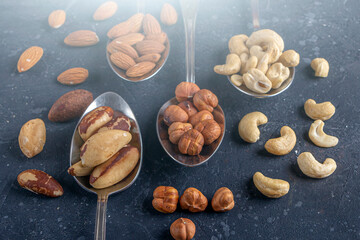 Assortment of various types of nuts: cashew, hazelnuts, almonds, brazil nuts on metal silver spoons on dark background. Healthy vegetarian snacks. Protein-containing food. Copy space for text