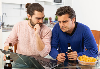 Friendly male meeting over beer at home, men looking at laptop and discussing. High quality photo