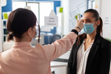 Woman using infrared thermometer measuring office worker temperature, during global epidemic with...