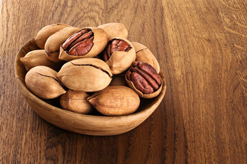 Pecan nuts in a bowl on a wooden background.