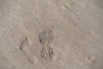 Human bare footprint and shoe print on a sand in nature environment.