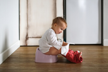 Funny kid Toddler sits on a pot with toilet paper, concept of teaching pot, child autonomy. Baby on...