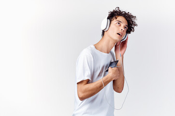 man with curly hair in white t-shirt listening to music with headphones phone technology