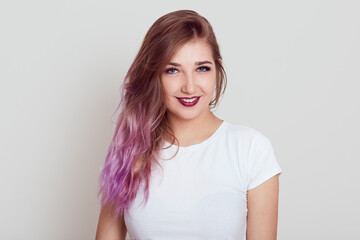 Obraz premium Young beautiful self confident lady in white casual t shirt looking at camera and expressing positive emotions, sees something pleasant, posing isolated over gray background.