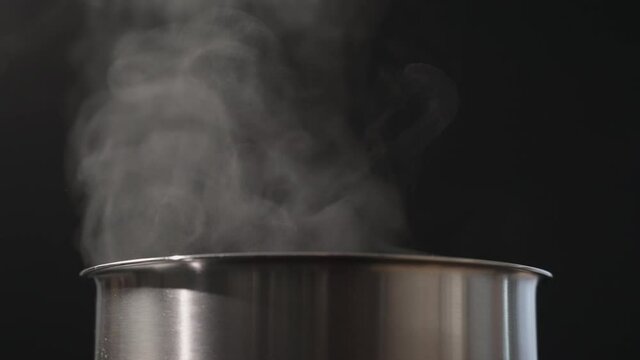 Slow motion blow rising steam from pot over black background