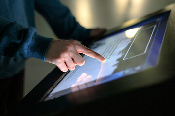 A boy uses the interactive touchscreen of an electronic multimedia kiosk at a museum of modern history. Education, training and technology concept - obrazy, fototapety, plakaty