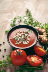Close-up of Indian Homemade fresh and healthy tomato soup garnished with fresh coriander leaves and ingredients and herbs, served in a black bowl over the marble top background. 