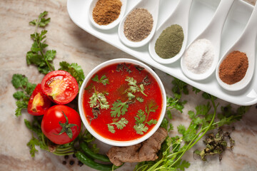 Close-up of Indian Homemade fresh and healthy tomato soup garnished with fresh coriander leaves and ingredients and herbs,  served in a white ceramic bowl with seasoning spices. 
