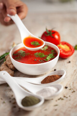 Close-up of Indian Homemade fresh and healthy tomato soup garnished with fresh coriander leaves and ingredients and herbs,  served in a white ceramic bowl with a spoon over marble top. 