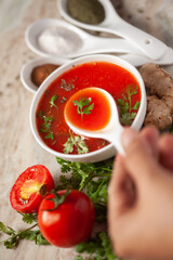 Close-up of Indian Homemade fresh and healthy tomato soup garnished with fresh coriander leaves and ingredients and herbs,  served in a white ceramic bowl with a spoon over marble top. 