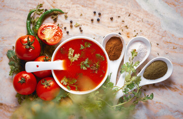 Close-up of Indian Homemade fresh and healthy tomato soup garnished with fresh coriander leaves and ingredients and herbs,  served in a white ceramic bowl with a spoon over marble top. 