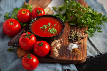Close-up of Indian Homemade fresh and healthy tomato soup garnished with fresh coriander leaves and ingredients and herbs, served in a black bowl over the wooden top background. 