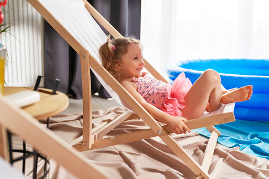 Happy little girl lying outdoor chair in swimwear at home