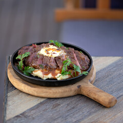 Frying pan with hot fried meat and vegetables on cutting board. Soft focus. Copy space.
