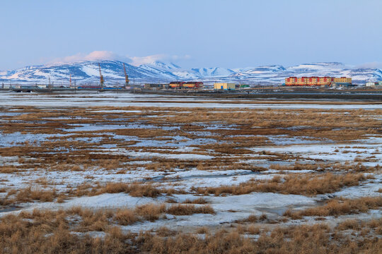 Spring arctic landscape. View of the tundra, colorful buildings and mountains. Mid-May in the Arctic. Melting snow in the tundra on the river bank. Tavayvaam village, Chukotka, Siberia, Russia.