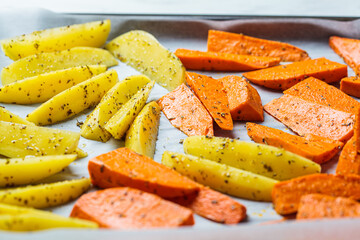 Raw potato and sweet potato wedges with spices on baking tray. Cooking healthy plant-based food.