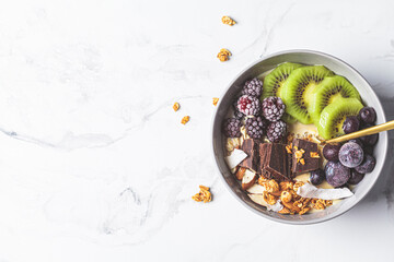 Overnight oatmeal bowl with kiwi, chocolate, berries and tahini, white marble background. Healthy vegan breakfast concept.