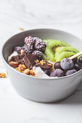 Overnight oatmeal bowl with kiwi, chocolate, berries and tahini, white marble background. Healthy vegan breakfast concept.