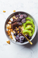 Overnight oatmeal bowl with kiwi, chocolate, berries and tahini, white marble background. Healthy...
