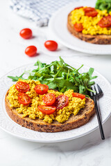 Tofu scrambled toast with tomatoes and arugula on white plate, white marble background. Vegan food concept.