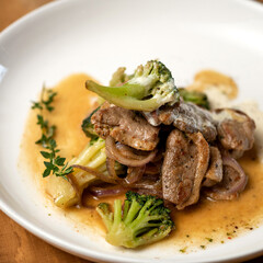 Pieces of stewed meat with sauce and broccoli on white plate. Close up shot, soft focus. Food concept. Square format or 1x1 for posting on social media.