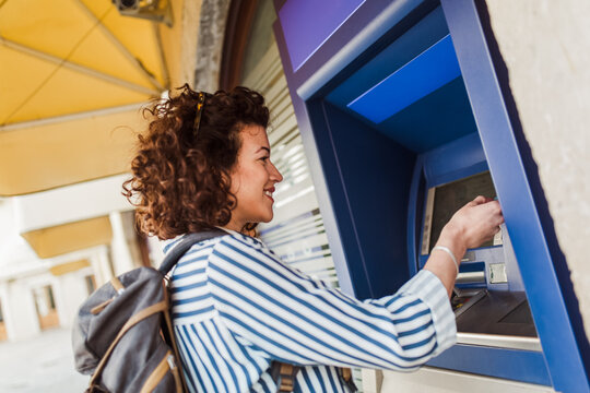 Attractive tourist woman uses a credit card near the ATM. The concept of tourism, travel, leisure.