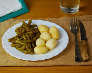 Tasty Green beans and potatoes on a plate on a brown napkin decorated with silver curtlery, aa glass of water and napkin holders