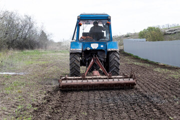 A tractor driver works the soil with a cultivator in the spring.