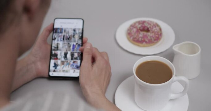 Woman at Home Sitting at Table With Coffee and Donut using Smartphone Scrolling Through Account  Feed. Girl Looks Social Network  Page On Mobile Phone. Woman Using Social Network on Smartphone.