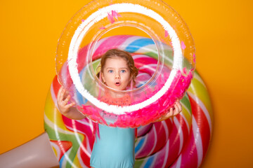 Funny little girl in swimming suit with swimming inflatable ring smiling having fun on yellow background.