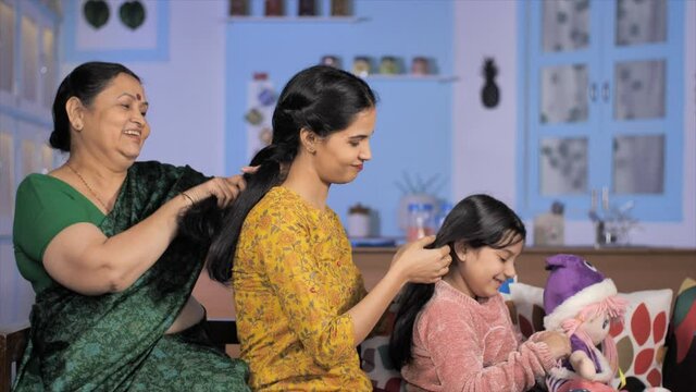Three generations of women making braided hair at home - haircare. Family bonding in India. Medium shot of an adorable little girl copying her mother and grandmother and styling her doll's hair