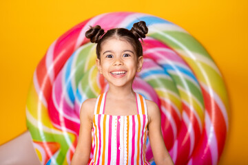 Happy excited arab child girl in colorful striped dress having fun on yellow background with lollipop