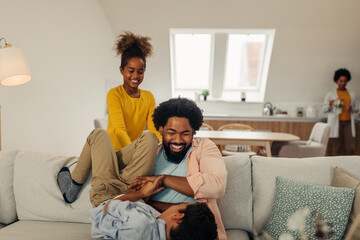 Afro family in the living room. Father tickling his children