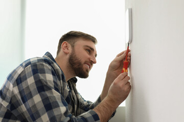 Man installing security alarm system on light wall at home