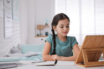 Little girl doing homework with tablet at table in bedroom