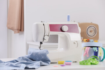 Modern sewing machine, fabric and accessories on table indoors