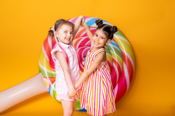 two happy little girls in colorful dress laughing holding hands having fun on yellow background