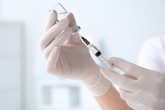 Doctor filling syringe with medication from vial on blurred background, closeup