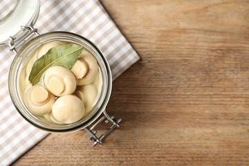 Jar with marinated mushrooms on wooden table, top view. Space for text