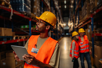 Warehouse worker using digital tablet looking up at tall shelves