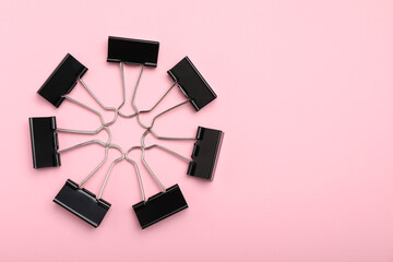 Black binder clips on pink background, flat lay. Space for text