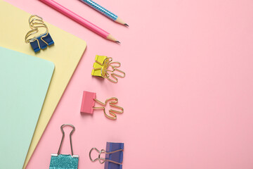 Binder clips and stationery on pink background, flat lay. Space for text